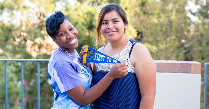 Two people holding a UCLA First to Go pennant